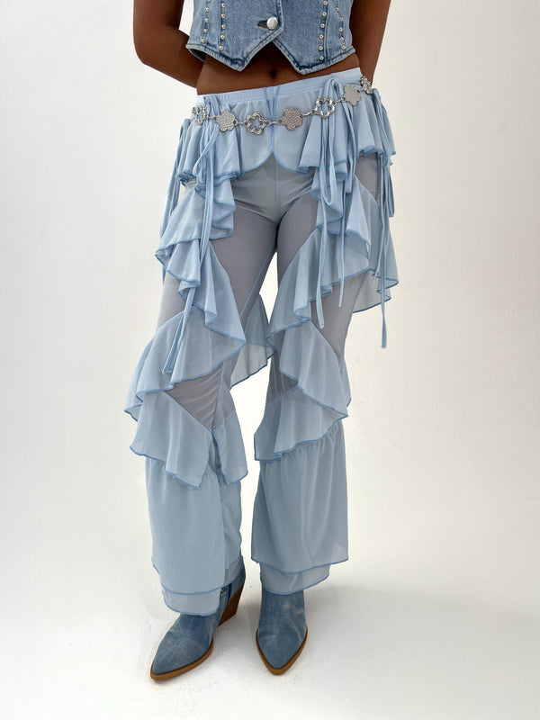 Person wearing a blue ruffled trousers with sheer elements on a white background