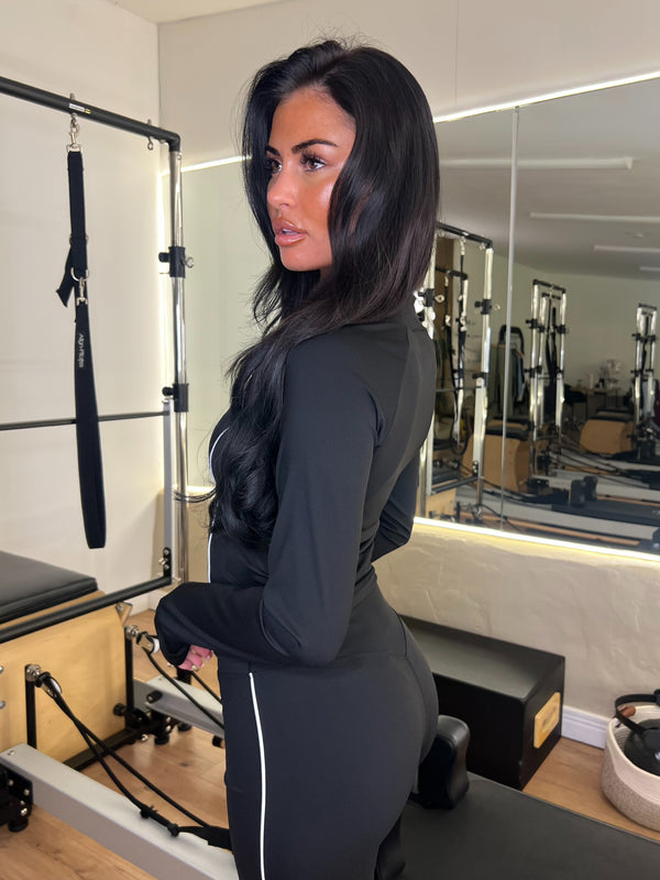 Woman in a black athletic outfit standing in a Pilates reformer room.