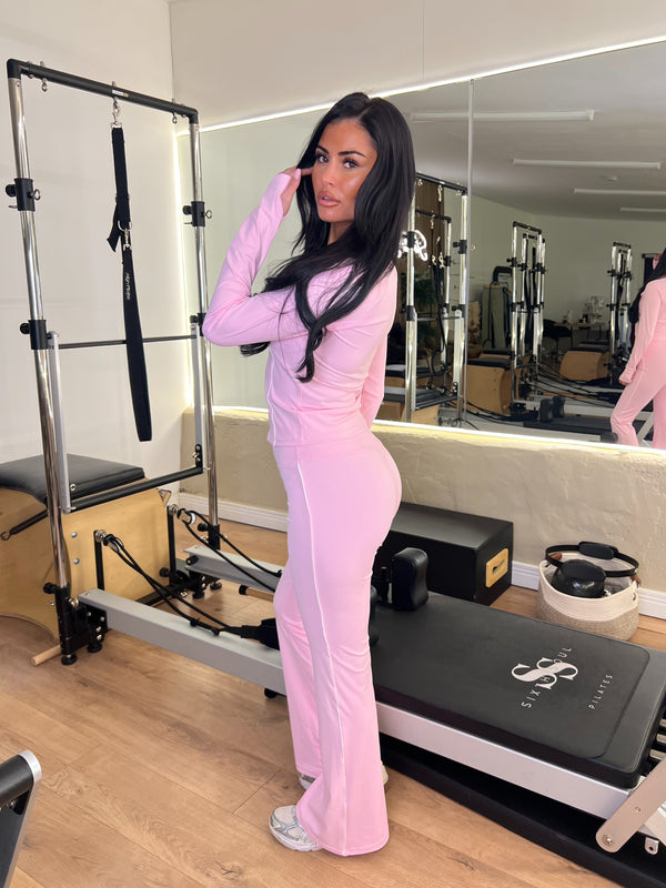 Woman in pink athletic wear standing in a Pilates reformer room.