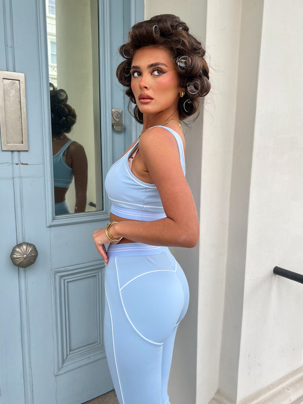 Woman in a light blue athletic outfit standing in front of a door.