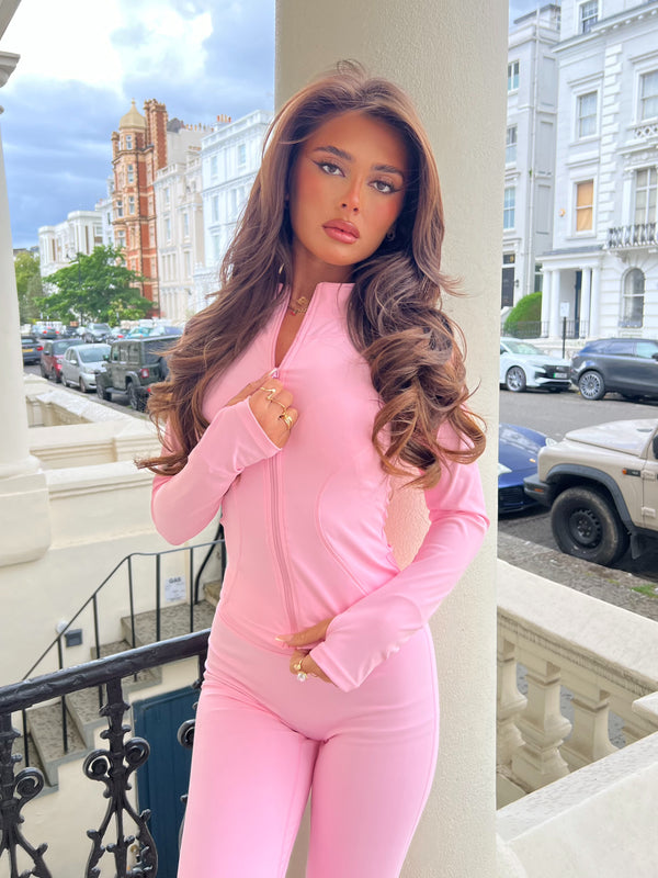 Woman in a pink outfit standing on a balcony with a cityscape background