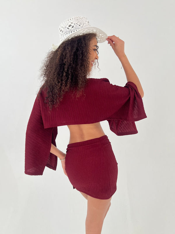 Woman wearing a burgundy outfit with a white hat on a plain background