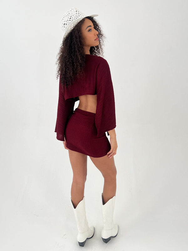 Lady in a burgundy outfit with white hat and boots on a white background