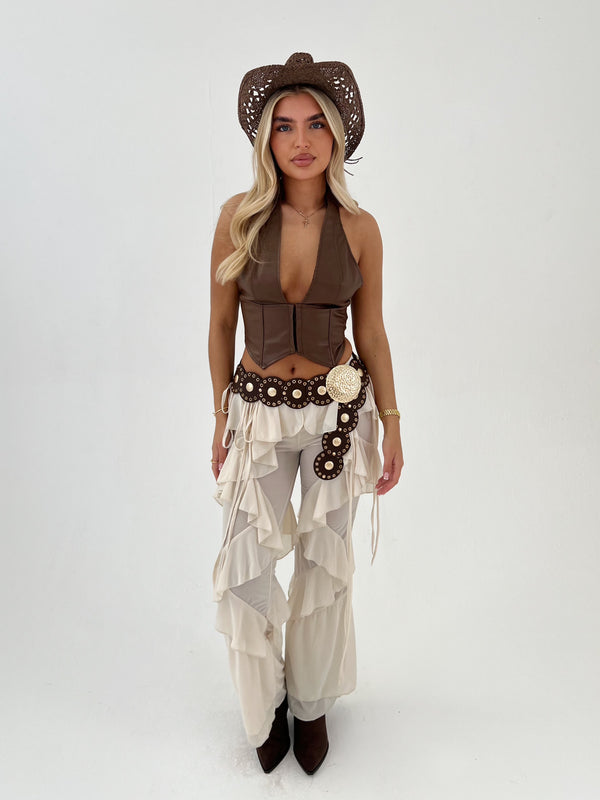 Woman wearing a cowboy outfit with a brown top, beige pants, and a hat on a white background