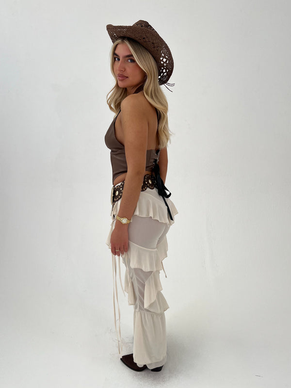 Woman wearing a brown top and beige trousers with a cowboy hat on a white background