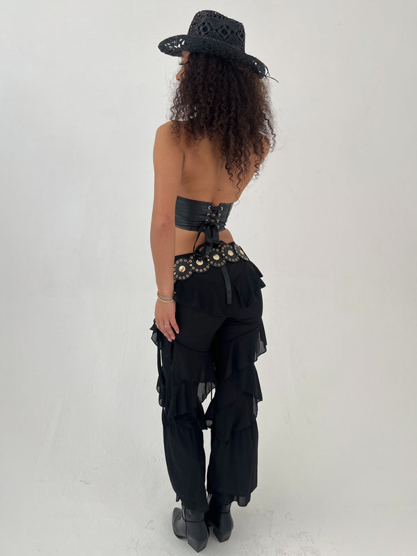 Person wearing a black outfit with layered trousers and hat on a white background