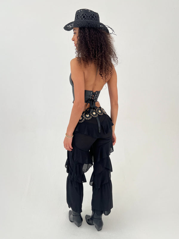 Person wearing a black outfit with ruffles and embellishments on a white background