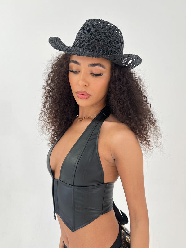 Woman wearing a black leather halter top and black straw hat on a white background