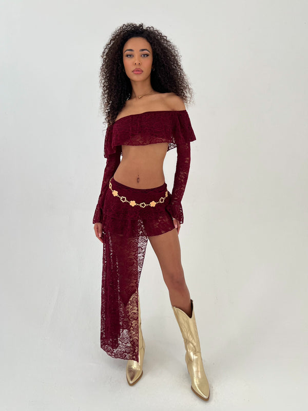Lady wearing burgundy lace top and skirt with a gold belt and gold cowboy boots on a white background