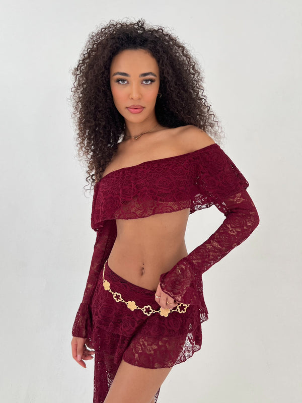 Lady wearing burgundy lace top and skirt with a gold belt on a white background