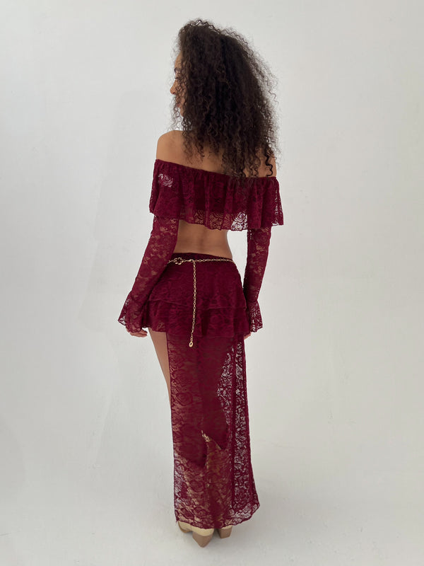 Lady wearing burgundy lace top and skirt with a gold belt on a white background