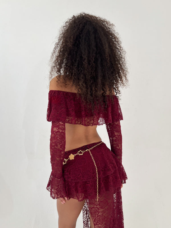 Lady wearing burgundy lace top and skirt with a gold belt on a white background