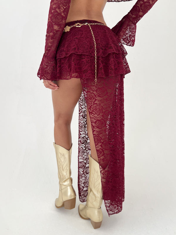 Lady wearing a burgundy skirt and gold belt and boots on a white background