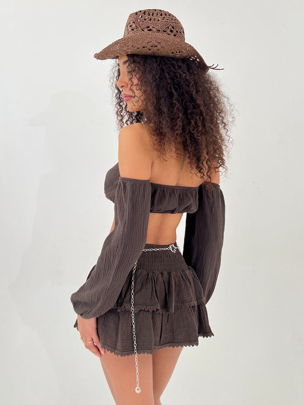 Woman wearing a brown off-shoulder top and skirt with a matching hat on a white background