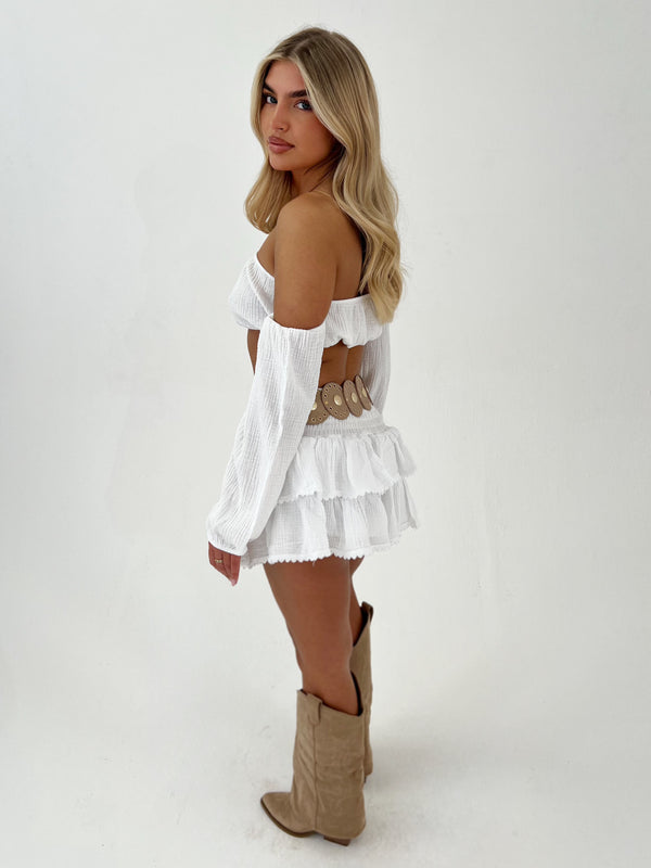 Woman wearing a white off-shoulder top and skirt with beige cowboy boots on a white background
