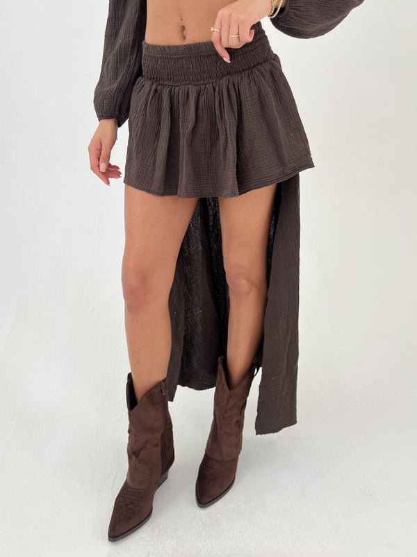 Person wearing a brown skirt with a high-low hem and matching boots on a white background