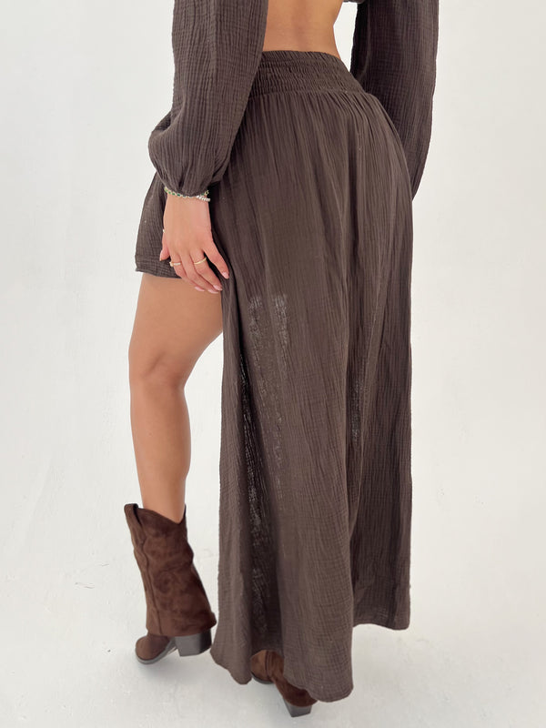 Person wearing a long brown skirt and matching top on a white background
