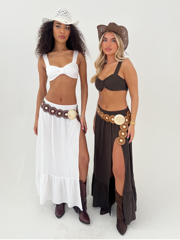 Two women wearing cowboy hats and long skirts with high slits on a white background