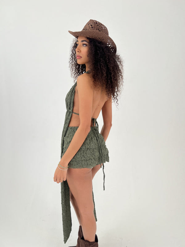 Woman wearing a green halter top and shorts with a brown cowboy hat on a white background