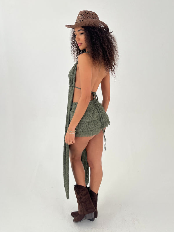 Woman wearing a green outfit, brown cowboy hat, and brown boots on a white background