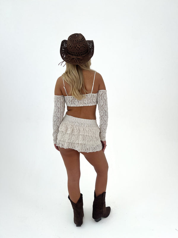 Person wearing a lace top, skirt, and cowboy hat on a white background