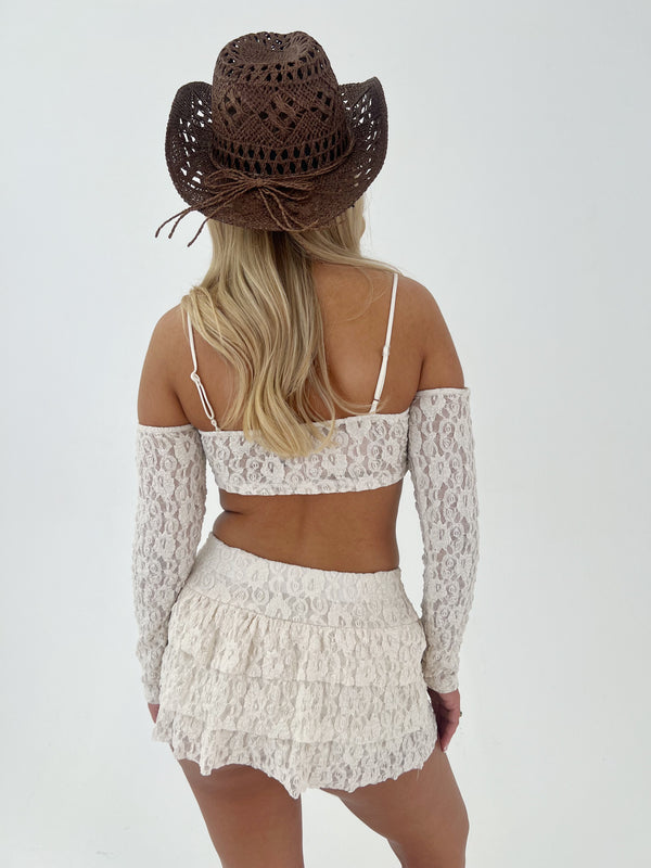 Person wearing a lace top and skirt with a cowboy hat on a white background
