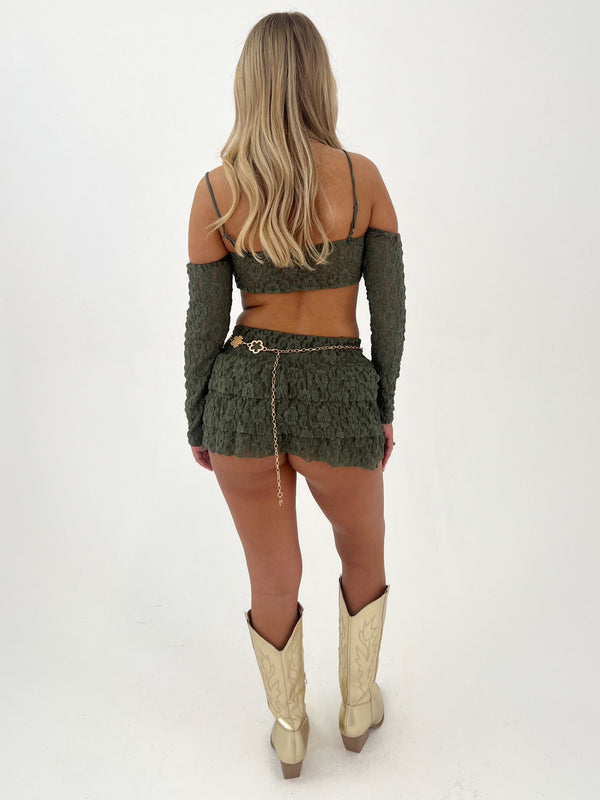 Person wearing a green outfit with a matching top and skirt, standing on a white background.