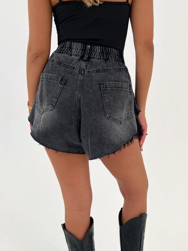 Person wearing black denim shorts and black boots on a white background