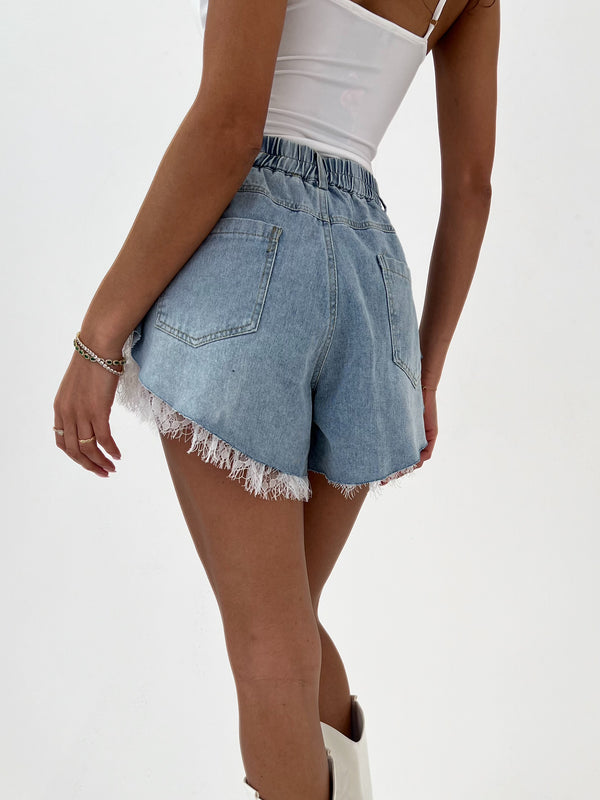 Denim shorts with lace trim worn by a person on a white background