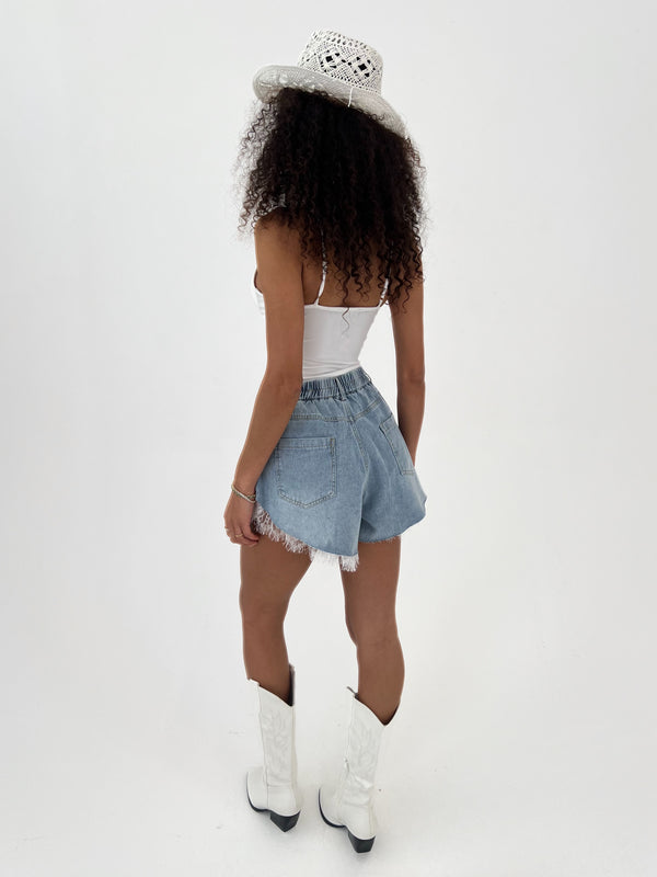 Person wearing a white top, denim shorts, and white boots on a plain background