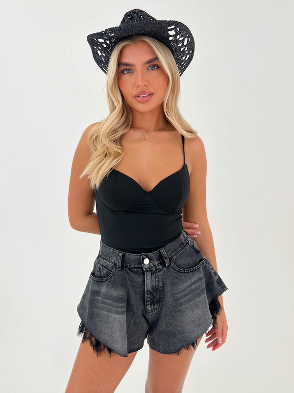 Woman wearing a black crop top and denim shorts with a black crochet hat on a white background