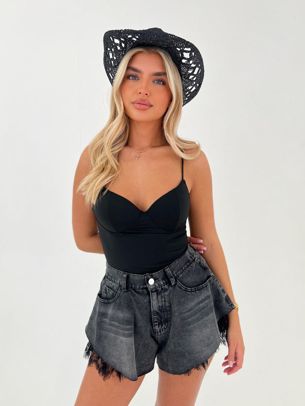 Woman wearing a black top and denim shorts with a black hat on a white background