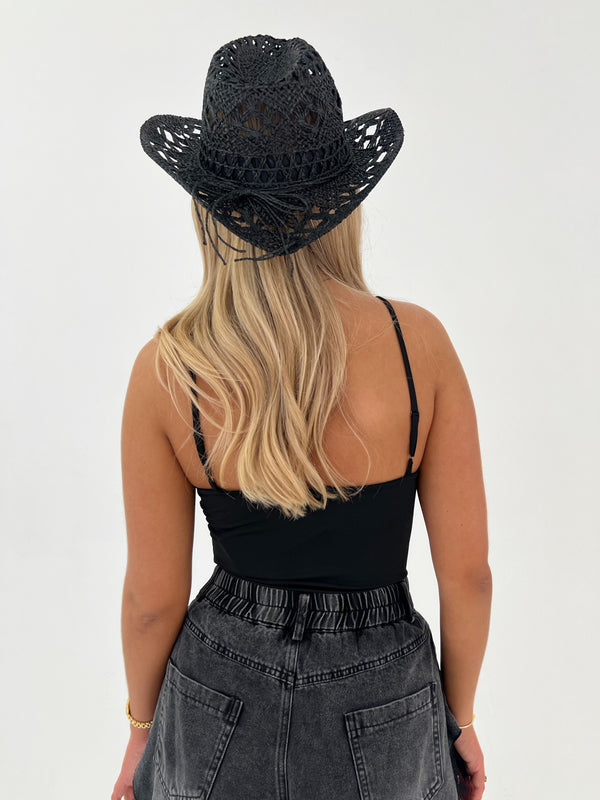 Person wearing a black lace hat, black tank top, and gray pants on a white background