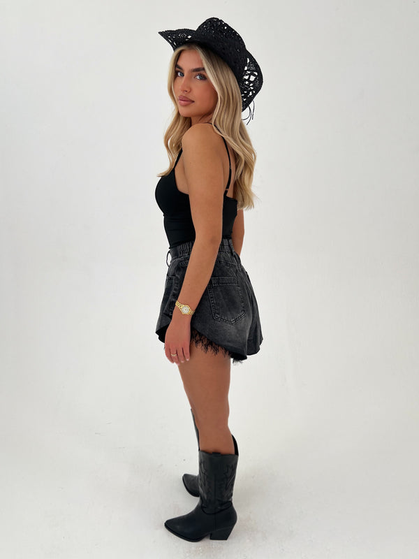 Woman wearing a black outfit with a hat and boots on a white background