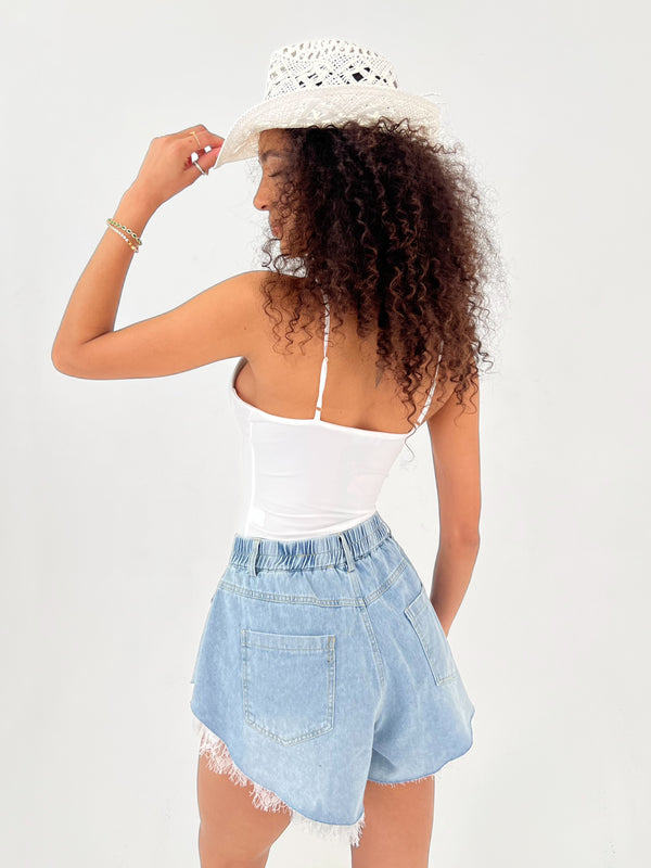 Woman wearing a white top and light blue denim shorts with a white hat on a plain background