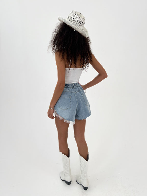Person wearing a white top, denim shorts, and white boots with a white hat on a white background