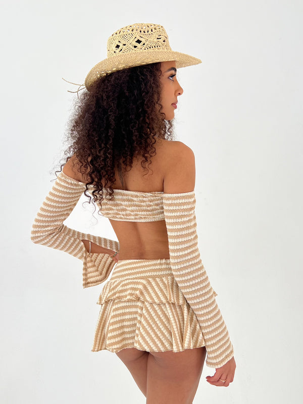 Woman wearing a beige and white striped outfit with a wide-brimmed hat on a white background