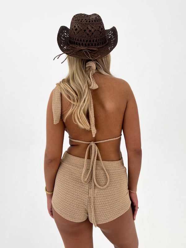 Person wearing a beige crochet top and shorts with a matching hat on a white background