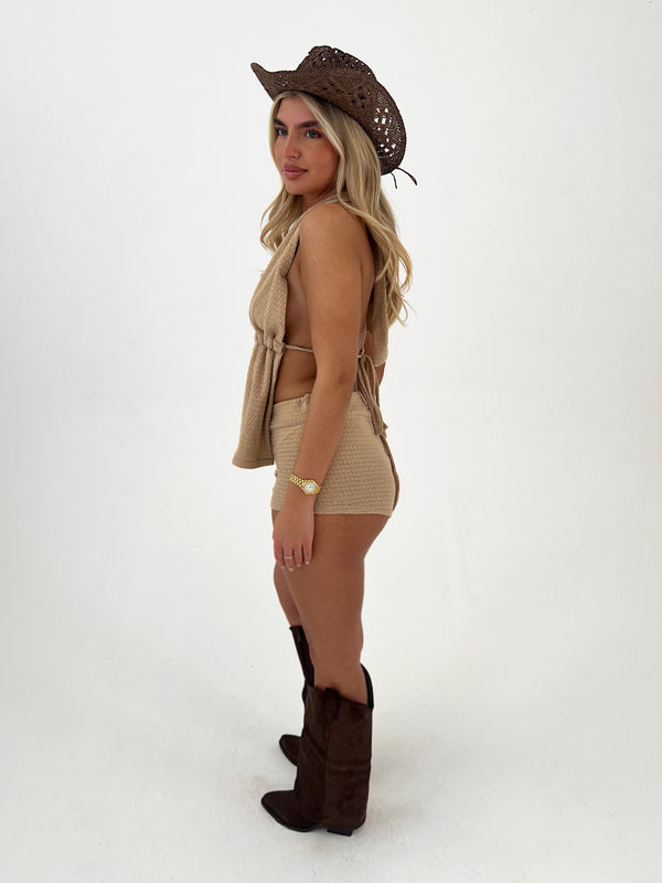 Woman wearing a beige outfit with a cowboy hat and boots on a white background