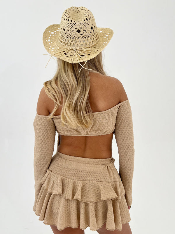 Woman wearing a beige crochet top and skirt with a matching hat on a white background