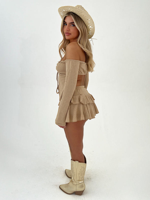 Woman wearing a beige outfit with a hat and boots on a white background