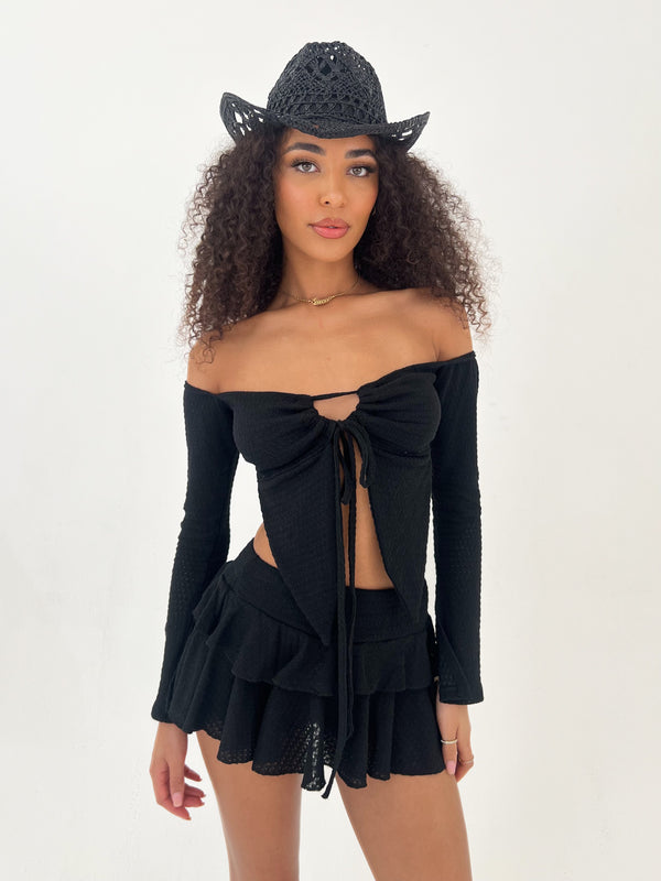 Woman wearing a black off-shoulder top and skirt with a matching hat on a white background