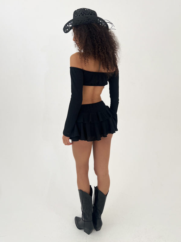 Person wearing a black outfit with long sleeves, skirt, and boots on a white background