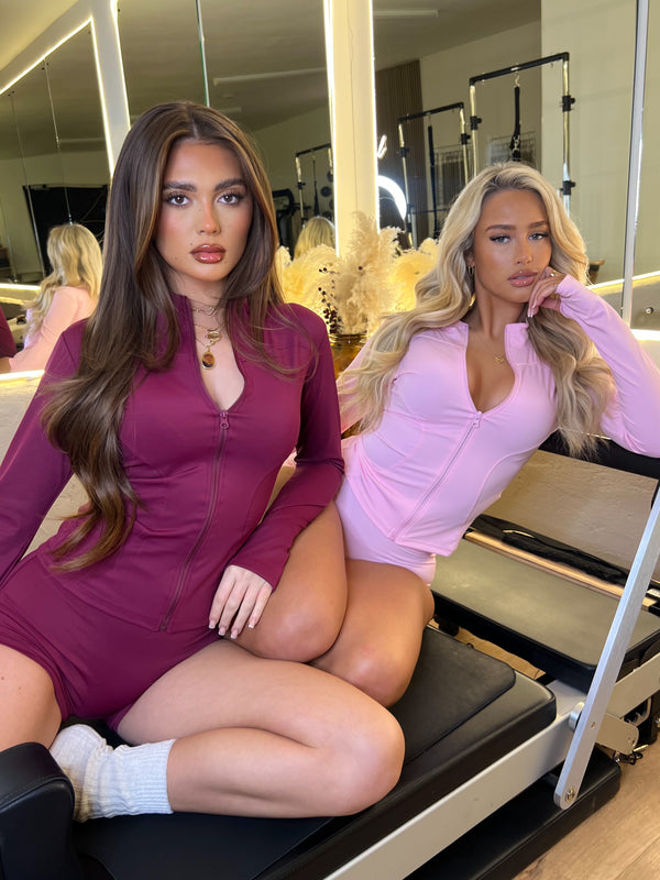 Two women in matching outfits sitting on a Pilates reformer machine.